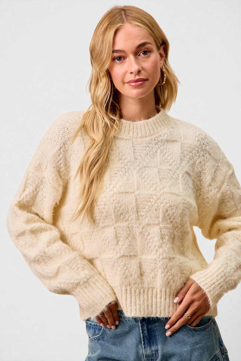 Woman wearing a cream knitted sweater and blue jeans against a white background