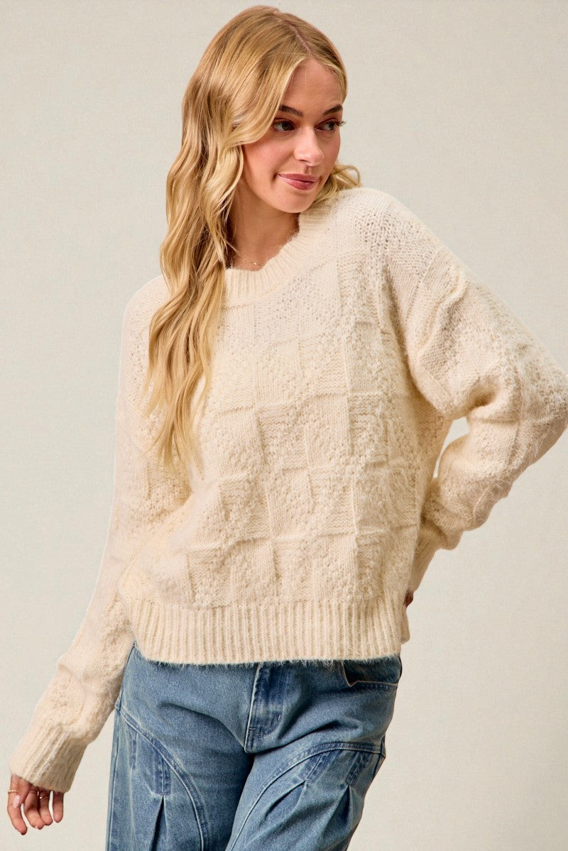 Woman wearing a cream sweater and blue jeans against a plain background