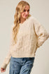 Woman wearing a cream sweater and blue jeans against a plain background