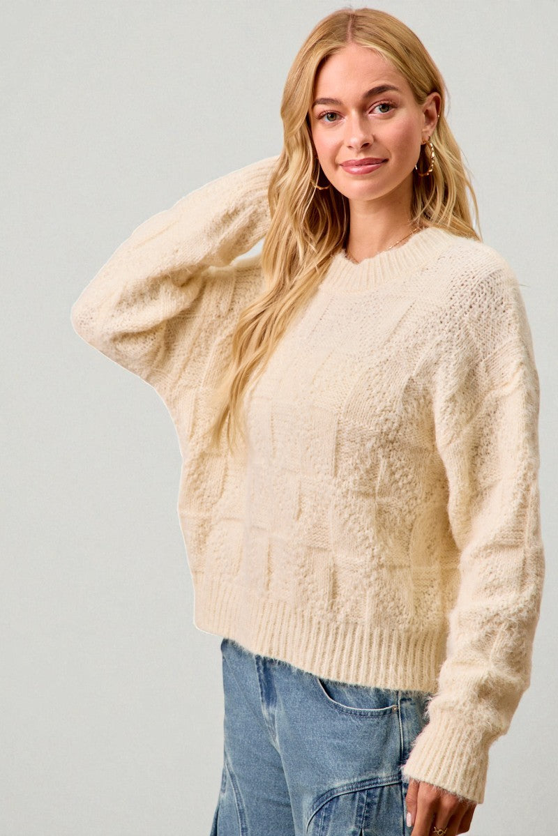 Woman wearing a cream sweater and blue jeans against a plain background