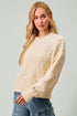Woman wearing a cream sweater and blue jeans against a light gray background