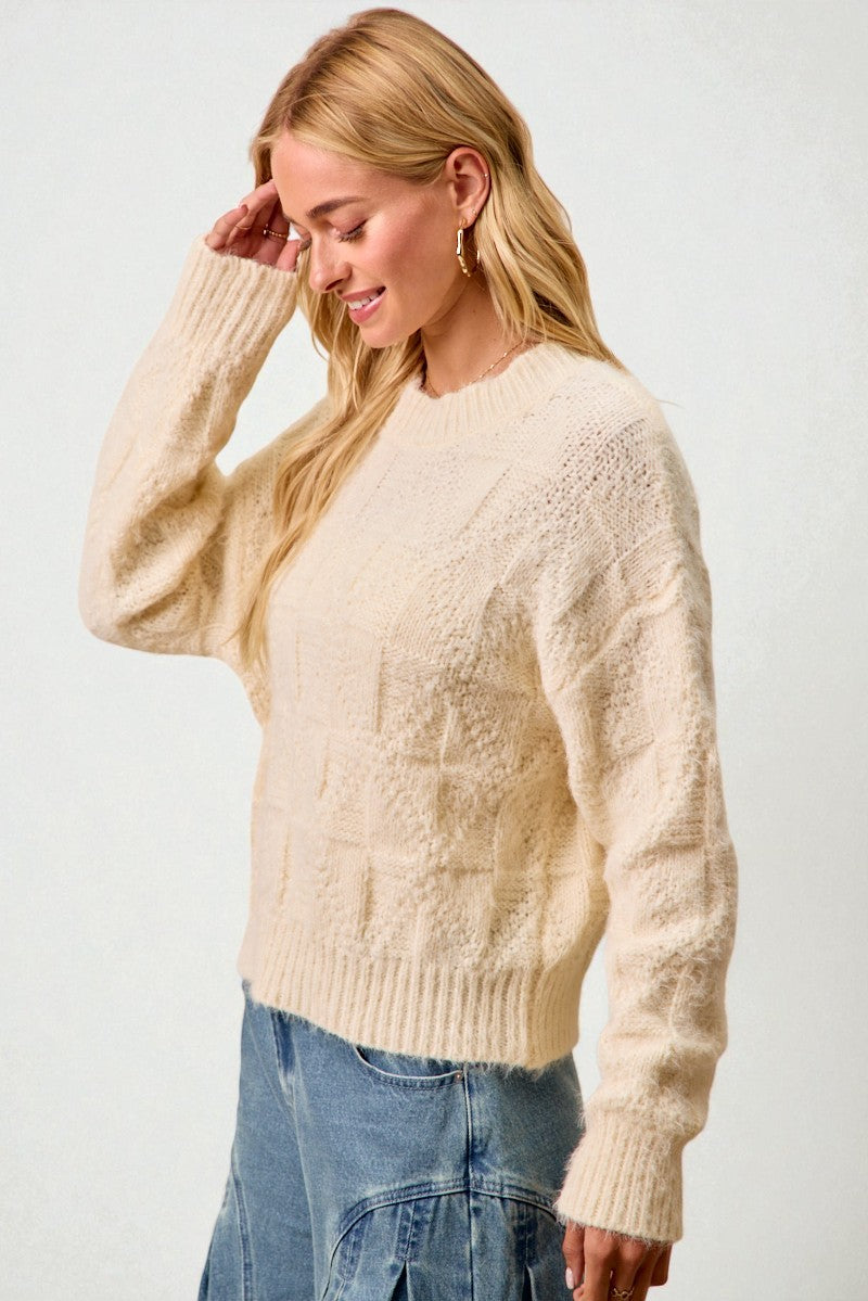 Woman wearing a cream sweater and blue jeans against a white background