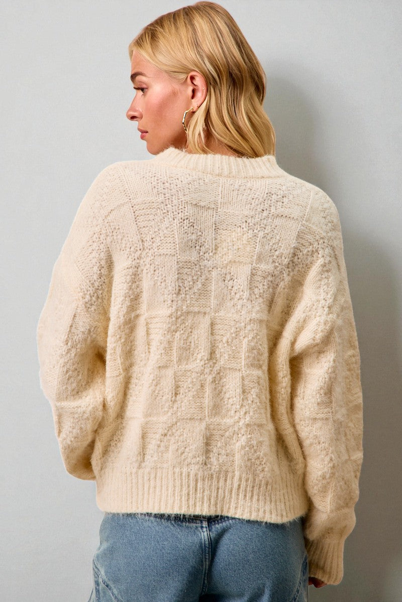 Person wearing a textured beige sweater against a plain background