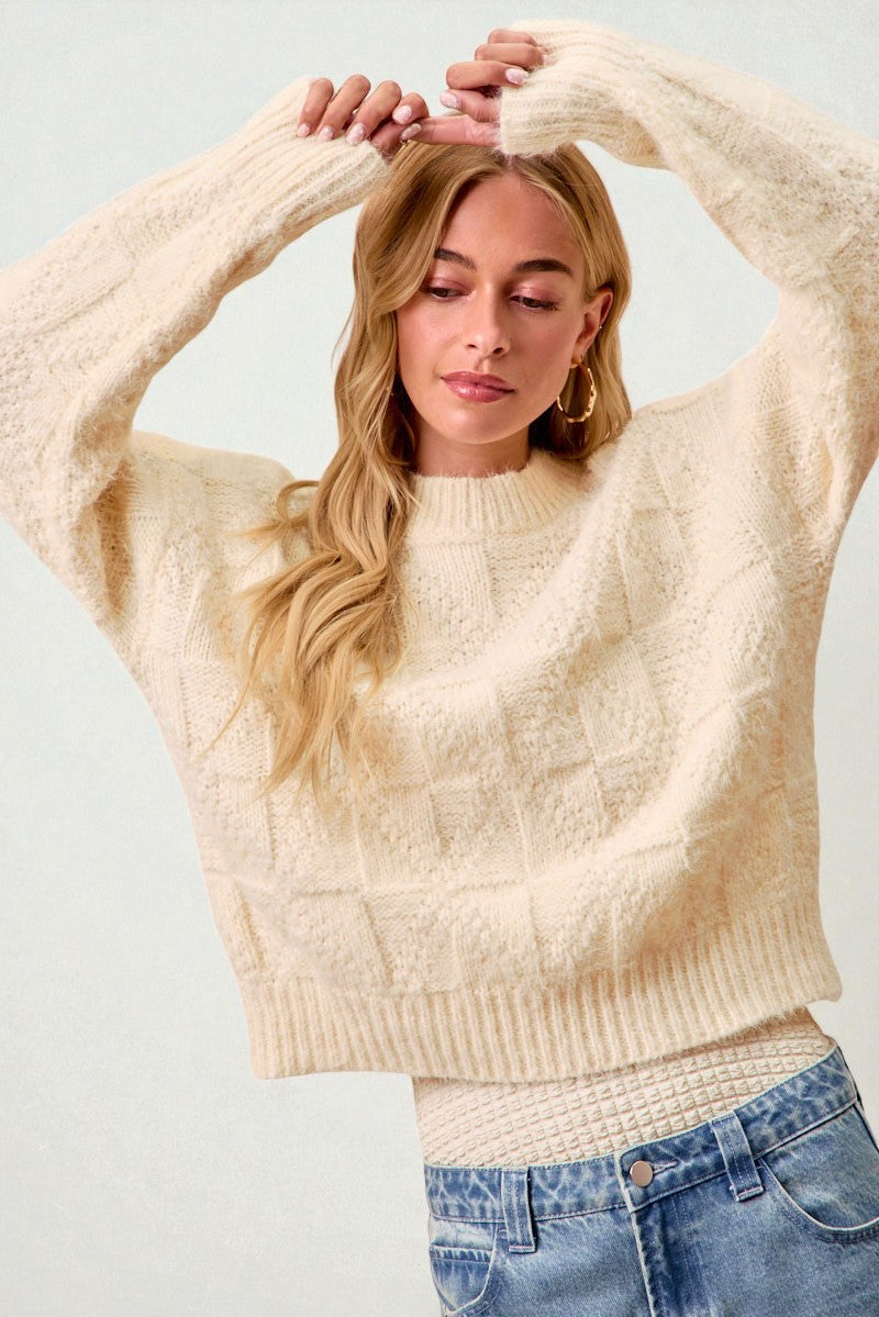 Woman wearing a beige sweater and denim shorts against a light background