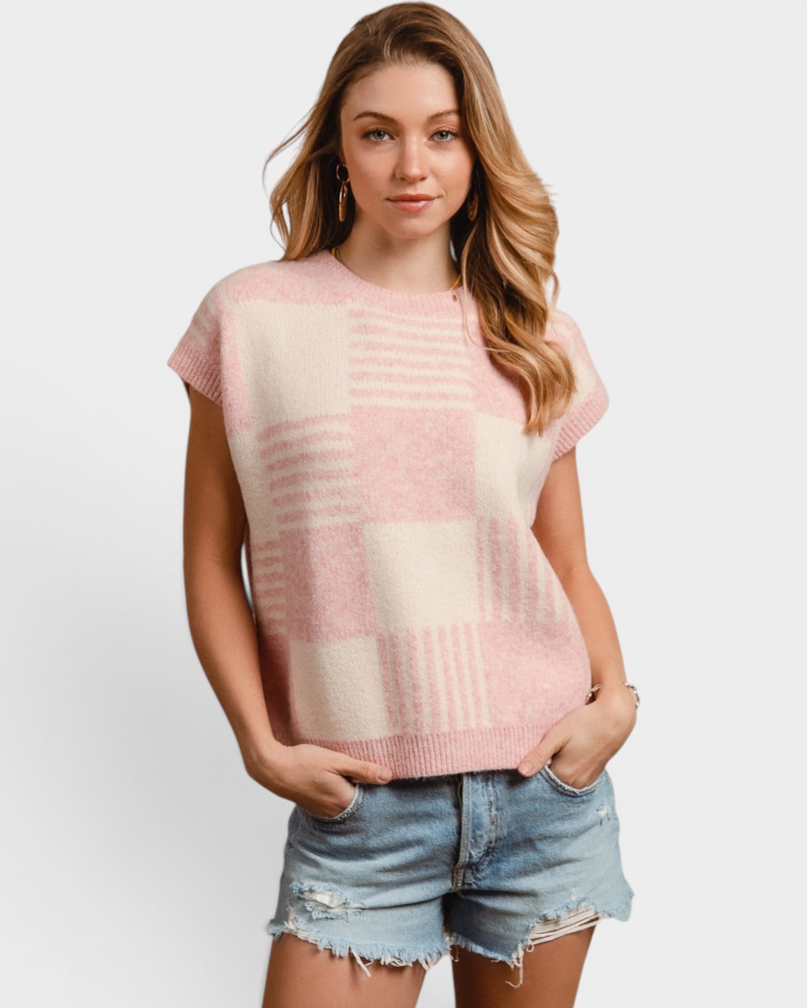 Woman wearing a pink and beige checkered sleeveless top with denim shorts on a white background