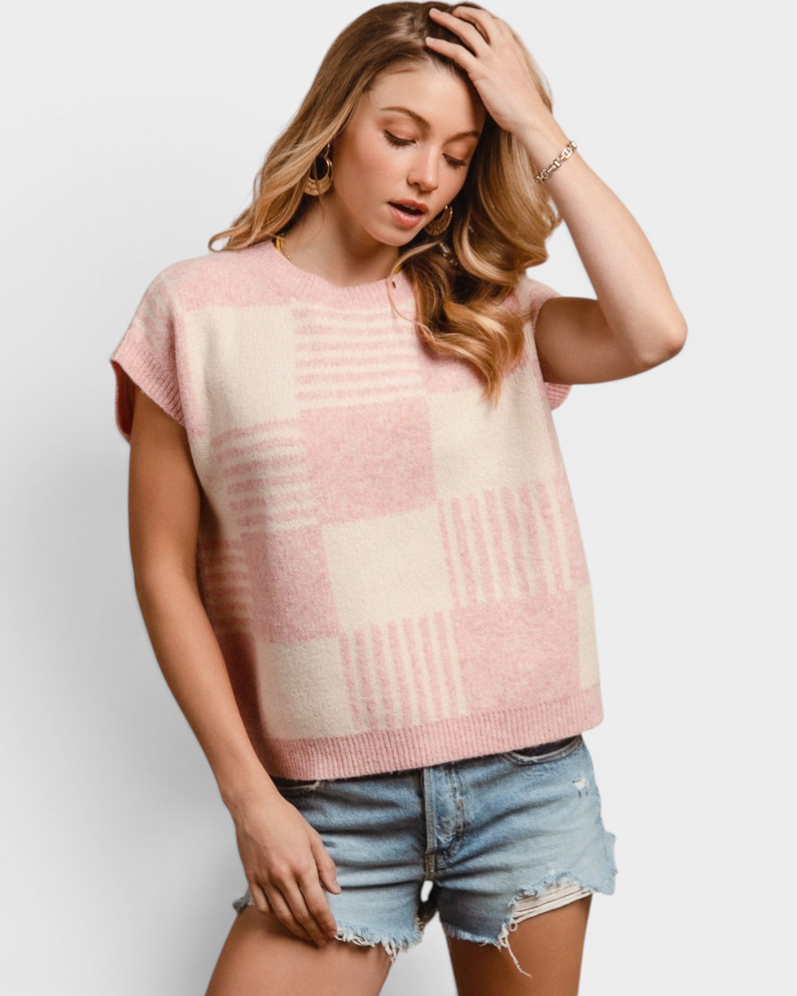 Woman wearing a pink and beige patterned sleeveless top with denim shorts on a white background