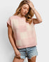 Woman wearing a pink and beige patterned sleeveless top with denim shorts on a white background