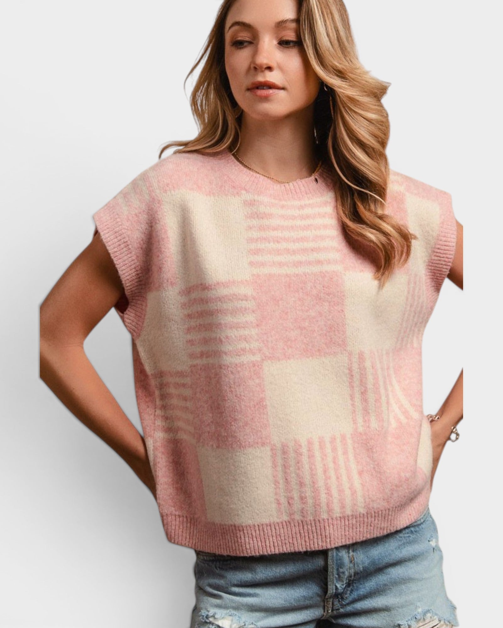Woman wearing a pink and beige checkered sleeveless sweater against a white background