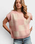 Woman wearing a pink and beige checkered sleeveless sweater against a white background
