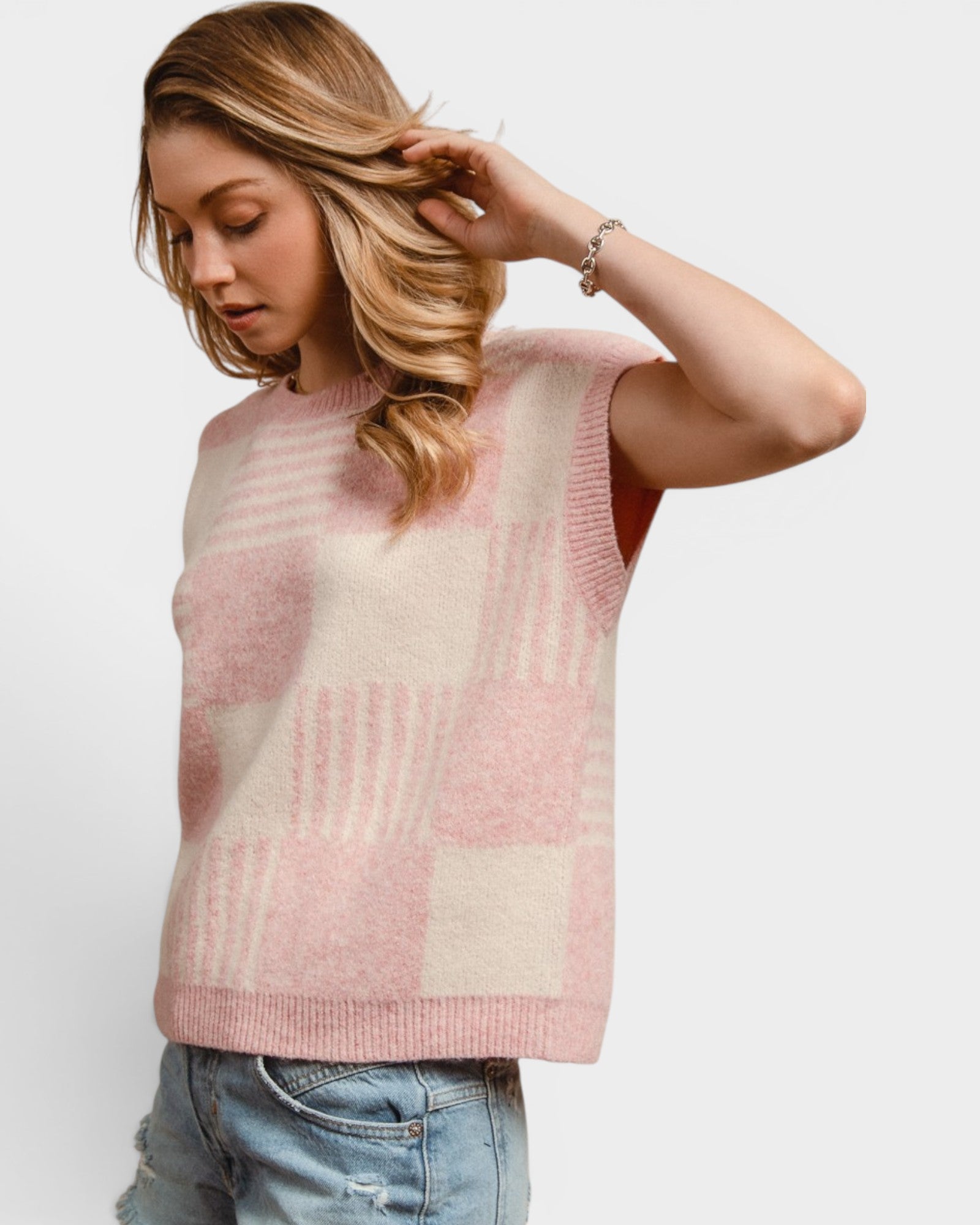 Woman wearing a pink and beige checkered sleeveless sweater against a white background