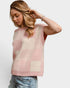 Woman wearing a pink and beige checkered sleeveless sweater against a white background
