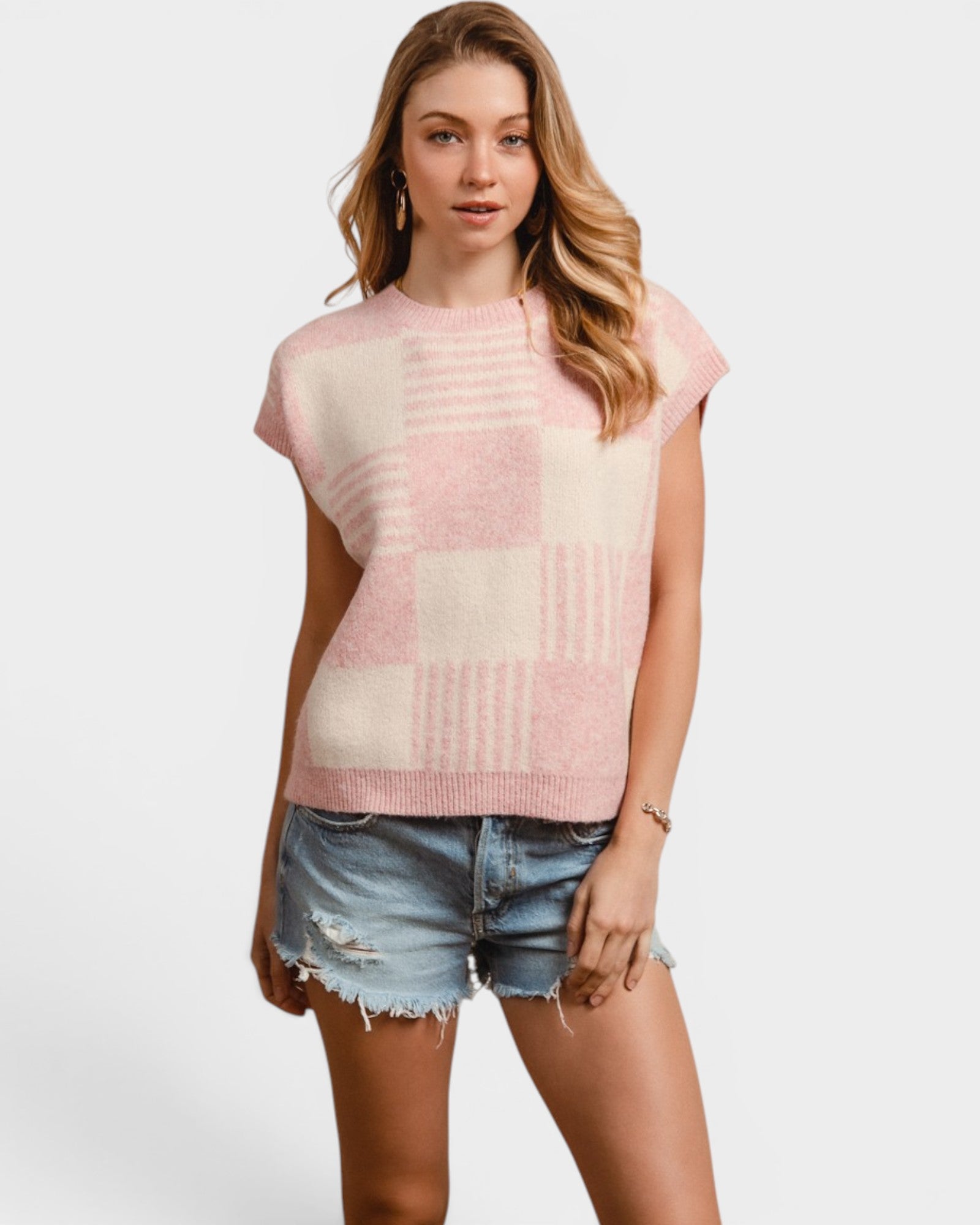 Woman wearing a pink and white checkered sleeveless top with denim shorts on a white background