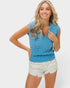 Woman wearing a blue sleeveless knitted top with white polka dots on a plain background