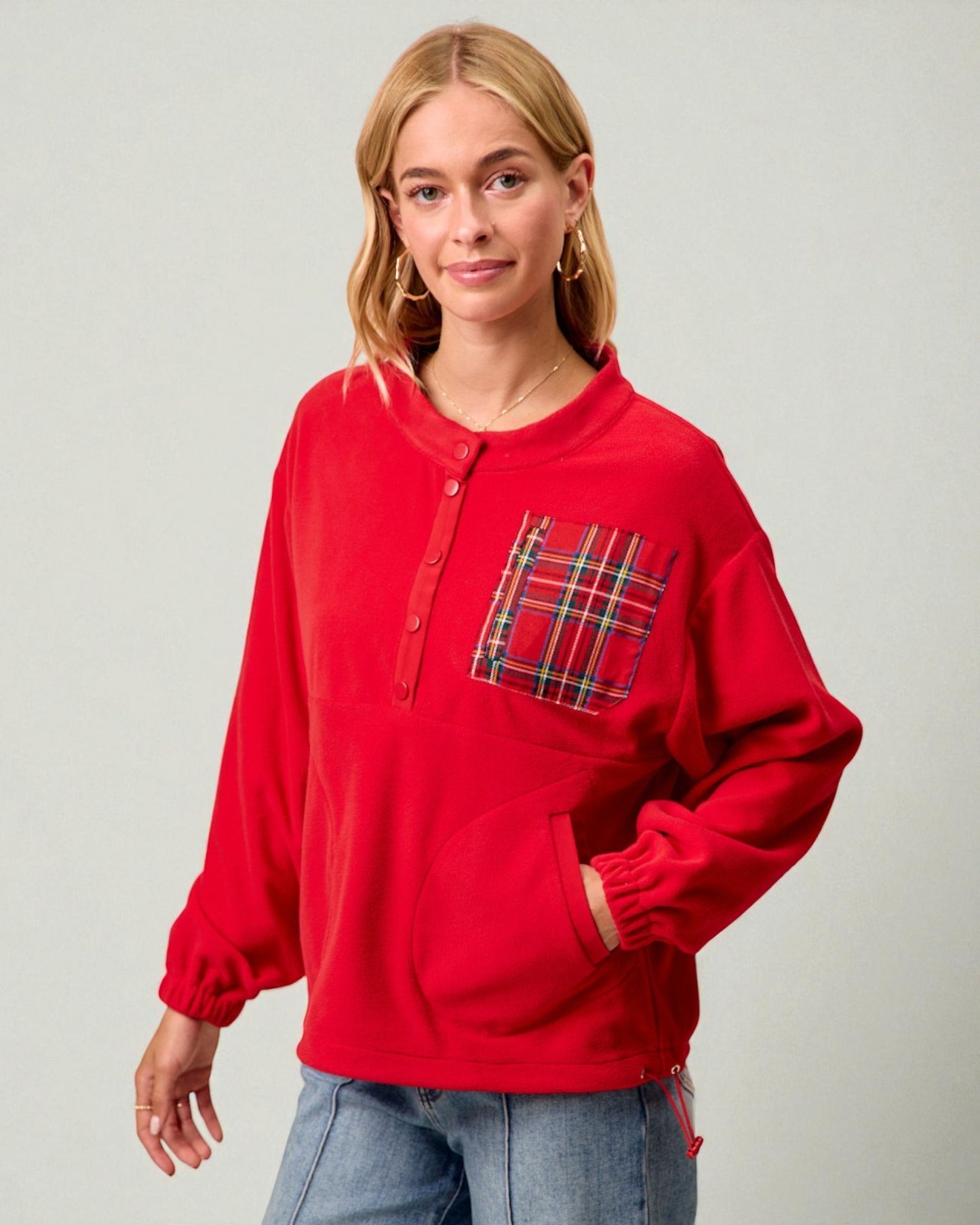 Person wearing a red long-sleeve shirt with a plaid pocket on a plain background