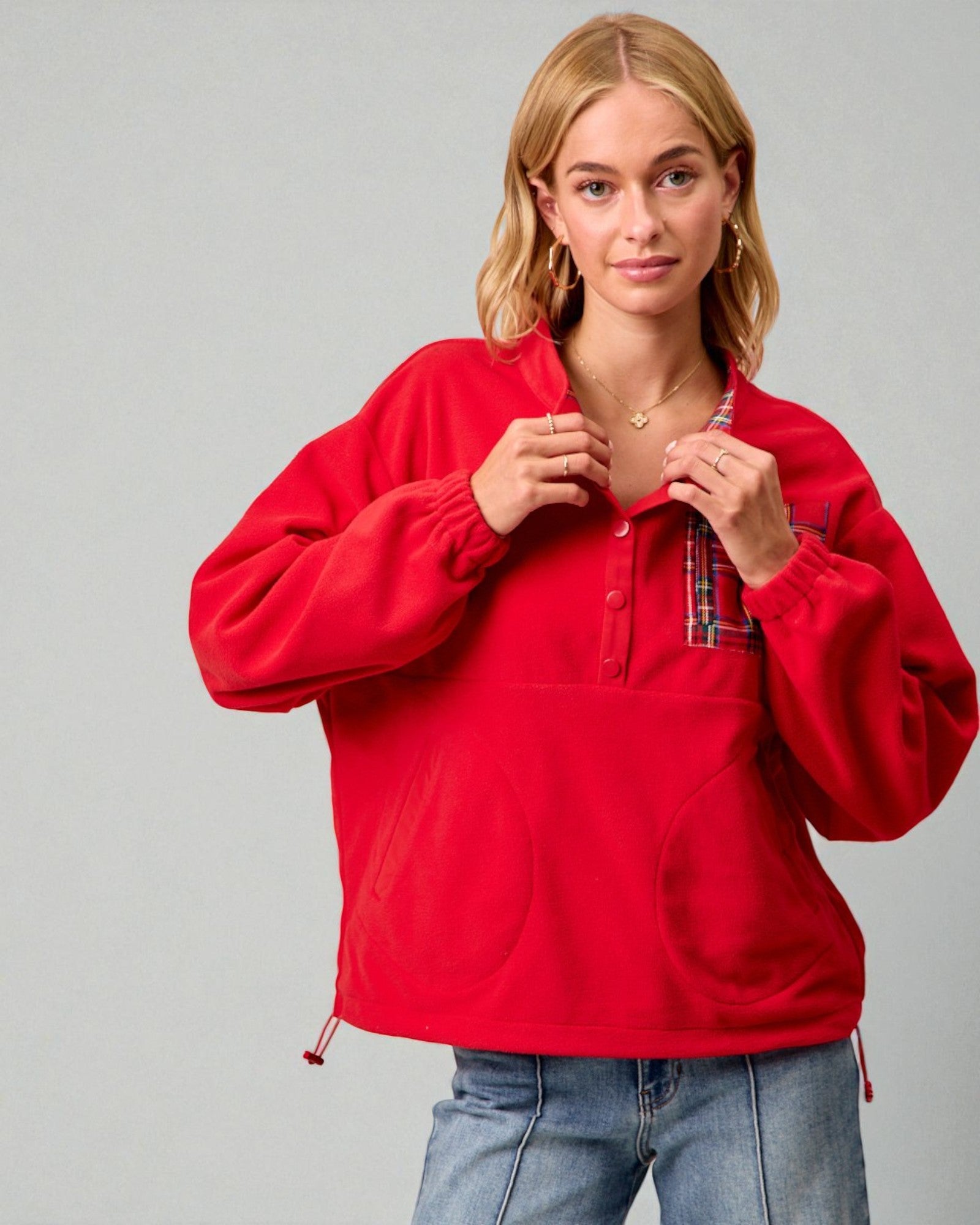 Woman wearing a red pullover with plaid lining on a gray background