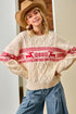 Woman wearing a cream sweater with red deer pattern and blue jeans indoors.