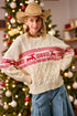 Woman wearing a cream sweater with red deer pattern in front of a decorated Christmas tree.