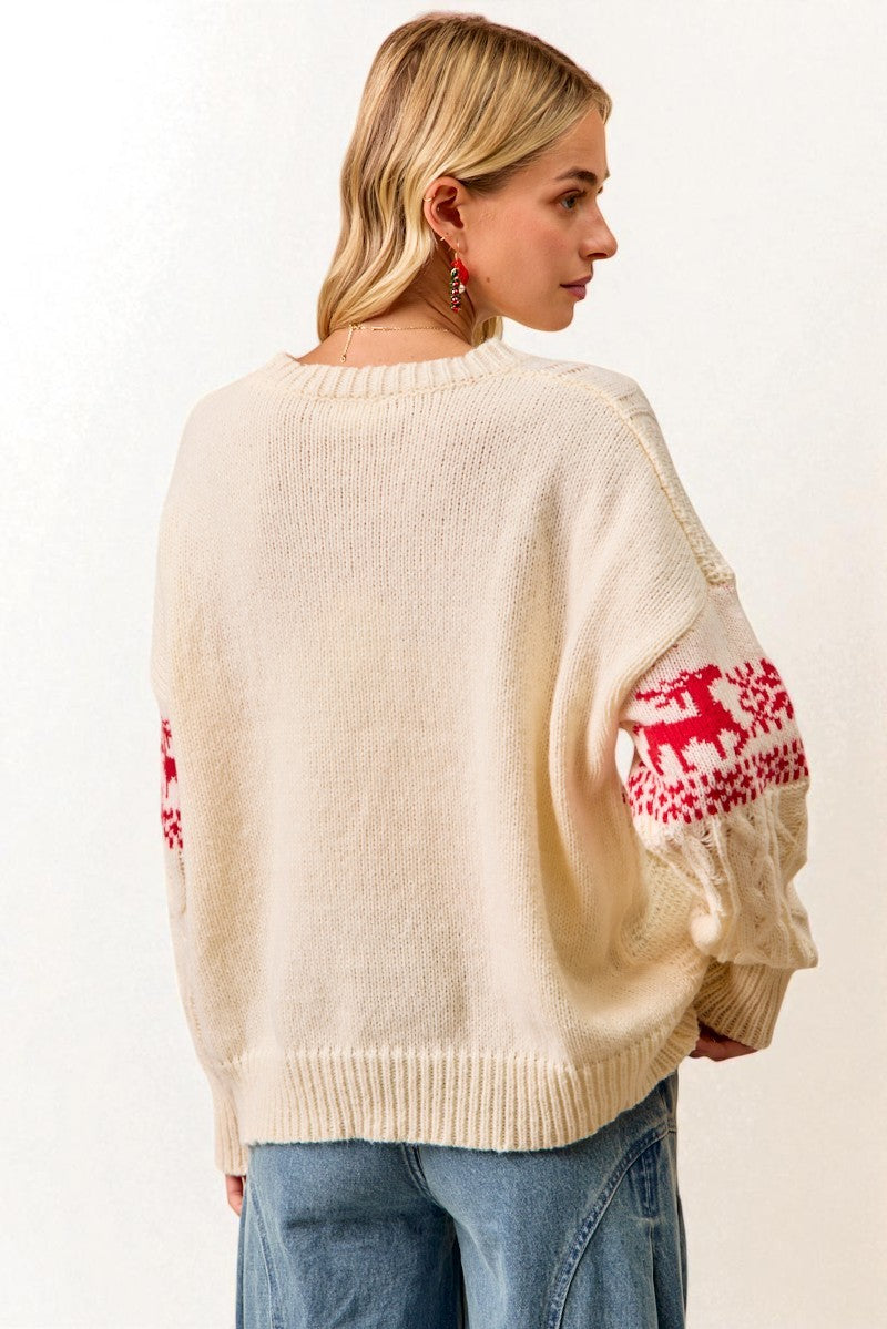 Woman wearing a cream sweater with red reindeer patterns on sleeves against a white background