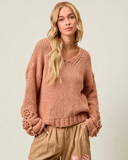 Woman wearing a pink knitted sweater and beige pants against a plain background
