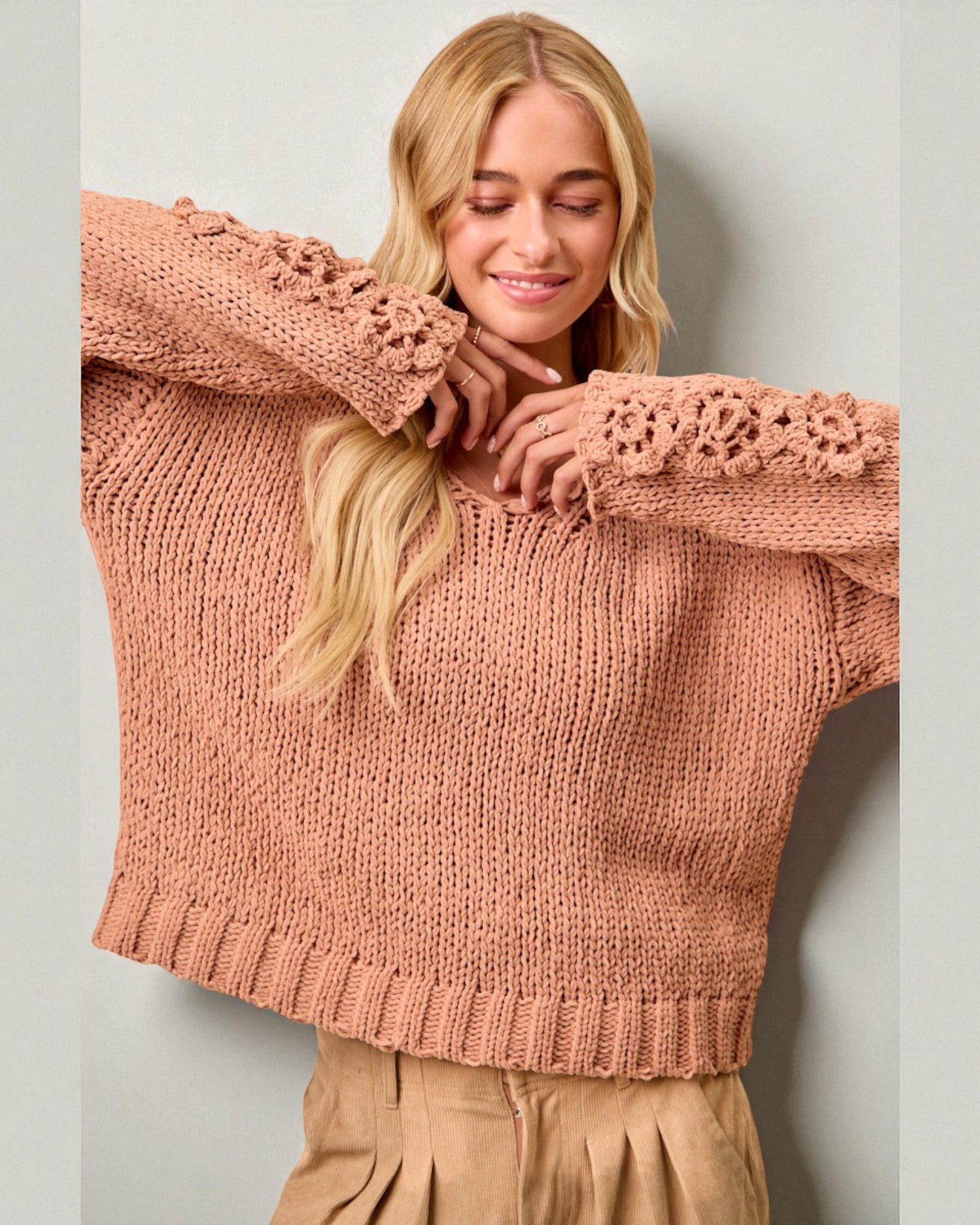 Woman wearing a pink sweater with lace details against a plain background