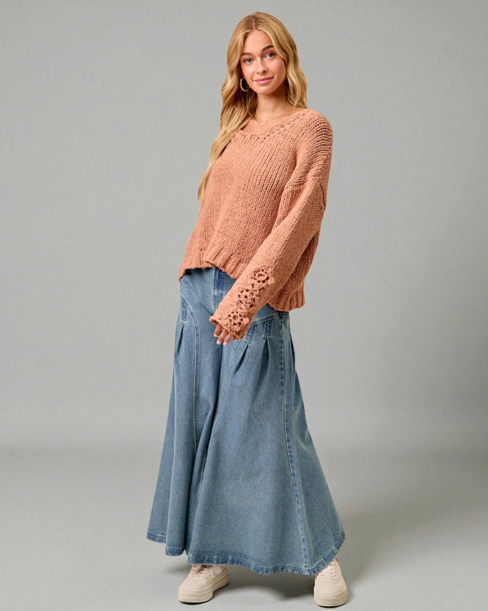 Woman wearing a pink sweater and blue denim skirt on a gray background