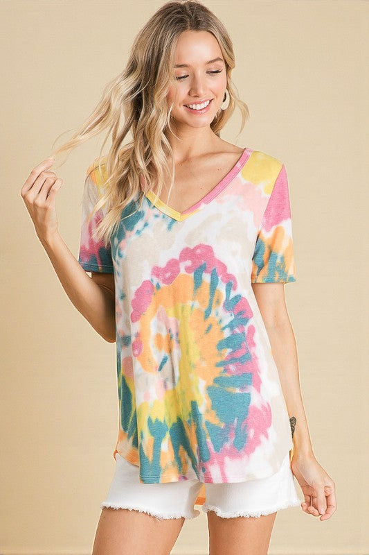 Woman wearing a colorful tie-dye shirt and white shorts on a beige background
