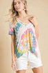 Woman wearing a colorful tie-dye top and white shorts on a beige background