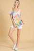 Woman wearing a colorful tie-dye shirt and white shorts on a beige background