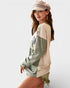Woman wearing a beige and green long-sleeve top with a cap on a white background