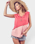 Woman wearing a pink and coral sleeveless top with denim shorts on a white background