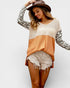 Woman wearing a color-blocked sweater with leopard print sleeves and denim shorts on a white background