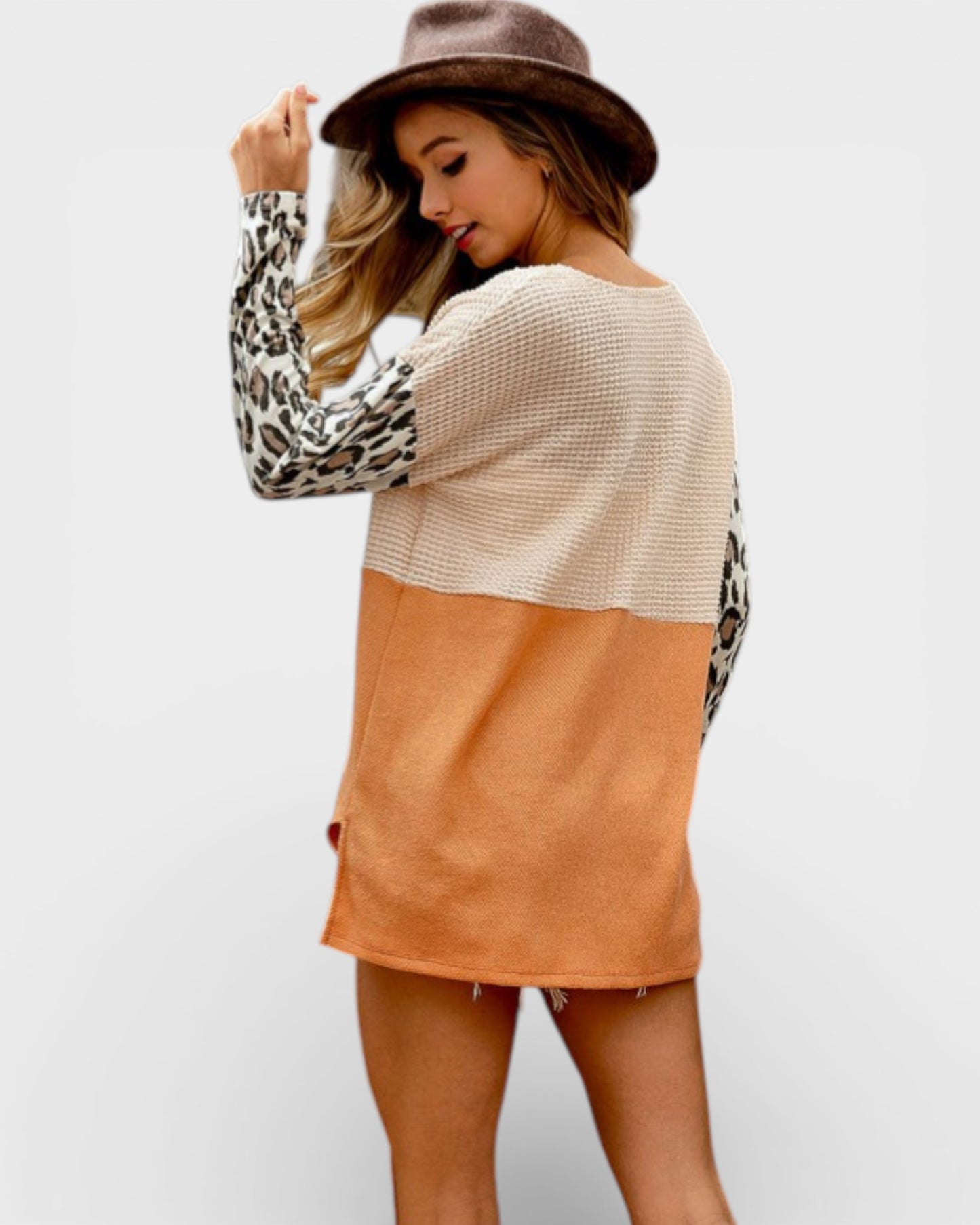 Woman wearing a color-blocked sweater with leopard print sleeves on a plain background