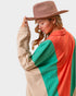 Woman wearing a beige hat and a colorful jacket with a neutral background