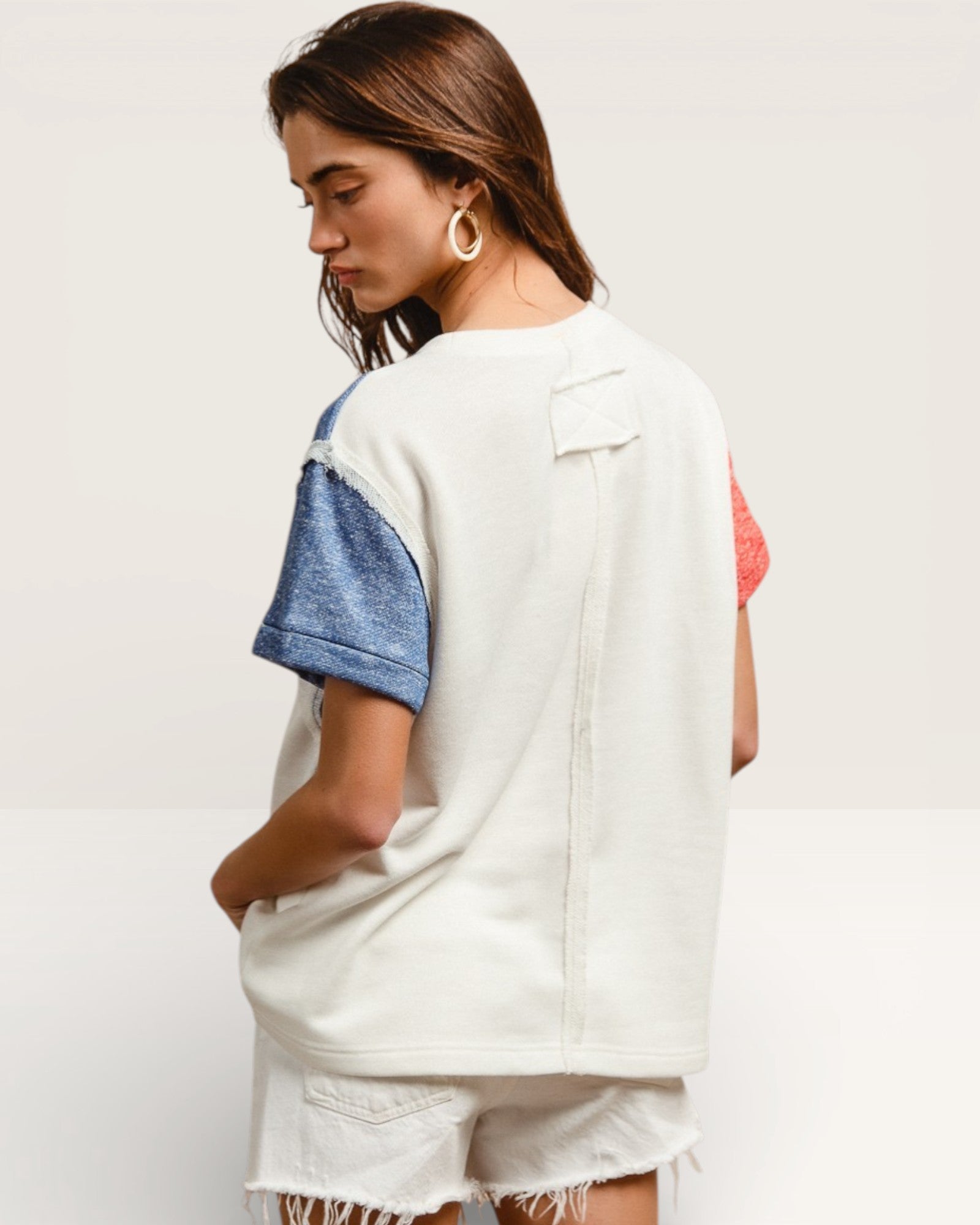 Woman wearing a white shirt with blue sleeves and denim shorts on a plain background