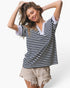 A woman modeling a short-sleeve striped t-shirt with a split V-neckline, featuring navy and white horizontal stripes with solid white trim. She is also wearing light beige distressed denim shorts against a clean white studio background.