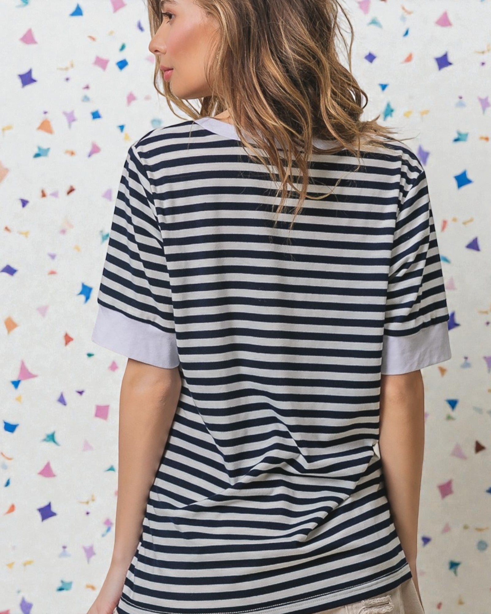 Woman wearing a black and white striped shirt against a colorful geometric patterned wall.