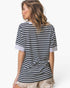 A woman shown from the back wearing a short-sleeve striped t-shirt with navy and white horizontal stripes, paired with light beige frayed shorts, against a plain white background.