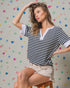 Woman wearing a striped shirt and shorts sitting on a stool against a polka dot wall.