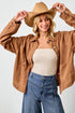 Woman wearing a brown jacket, beige top, and blue jeans with a tan hat against a white background