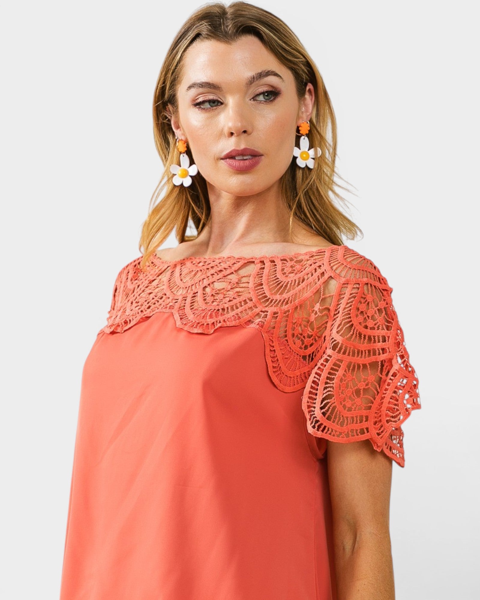 Woman wearing a coral dress with lace details on a white background