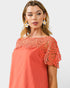 Woman wearing a coral dress with lace details on a white background
