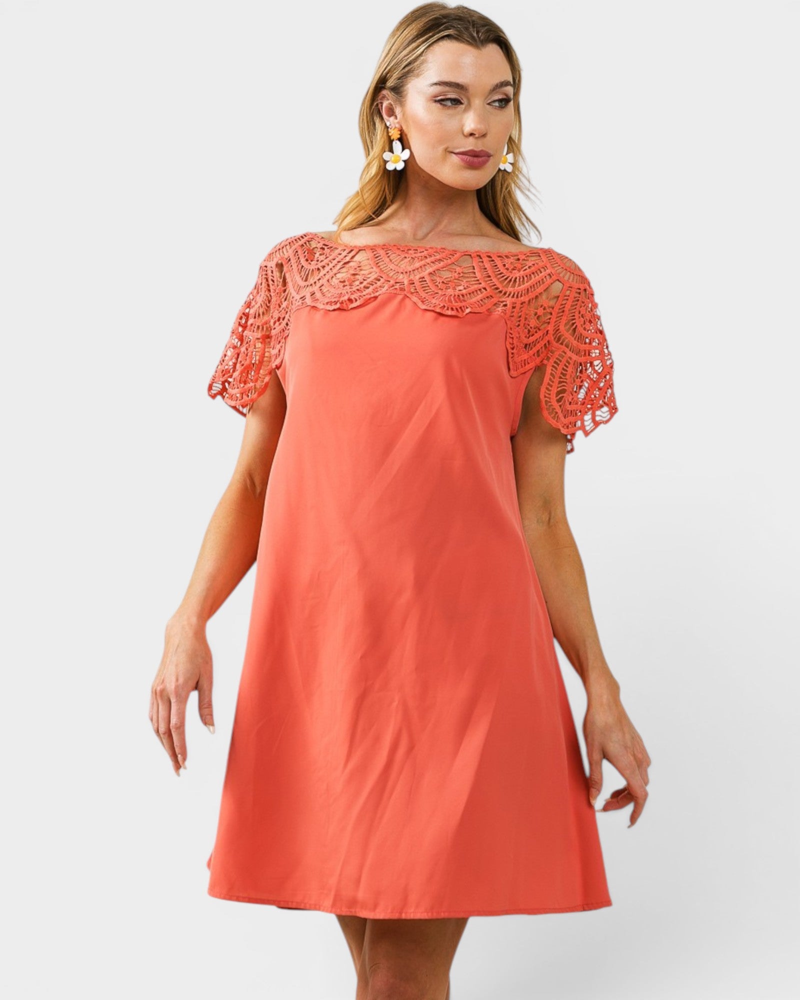 Woman wearing a coral dress with lace details on a white background