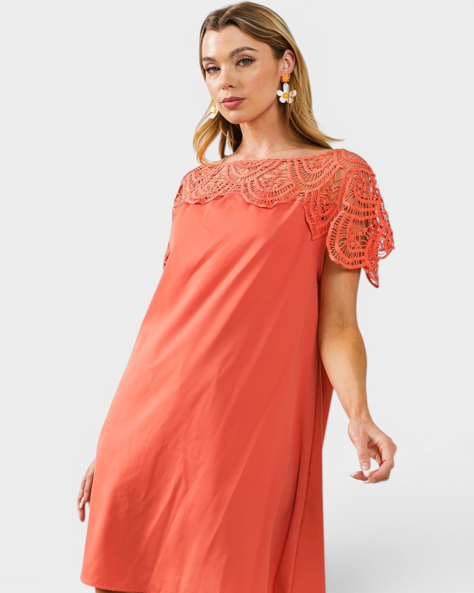 Woman wearing a coral dress with lace details on a white background