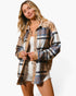 A woman modeling a long-sleeve plaid button-up shirt with leopard print shoulder yokes and leopard print trim, worn open over a white tank top and denim shorts against a plain white background.
