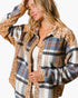 A woman wearing a long-sleeve button-up shirt with a plaid body and leopard-print collar, cuffs, and hem, layered over a white tank top against a plain white background.
