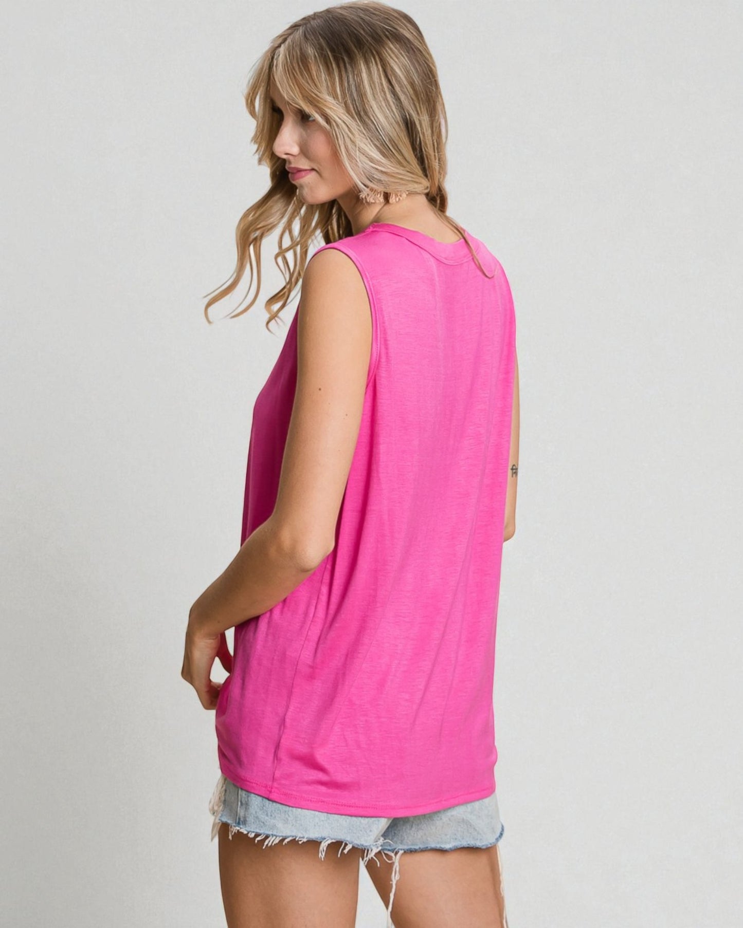 Woman wearing a bright pink sleeveless top and denim shorts on a plain background