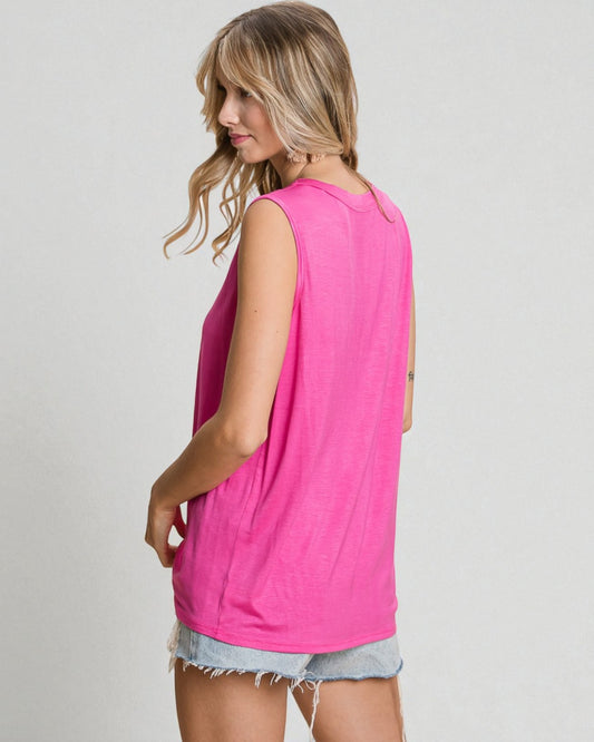 Woman wearing a bright pink sleeveless top and denim shorts on a plain background