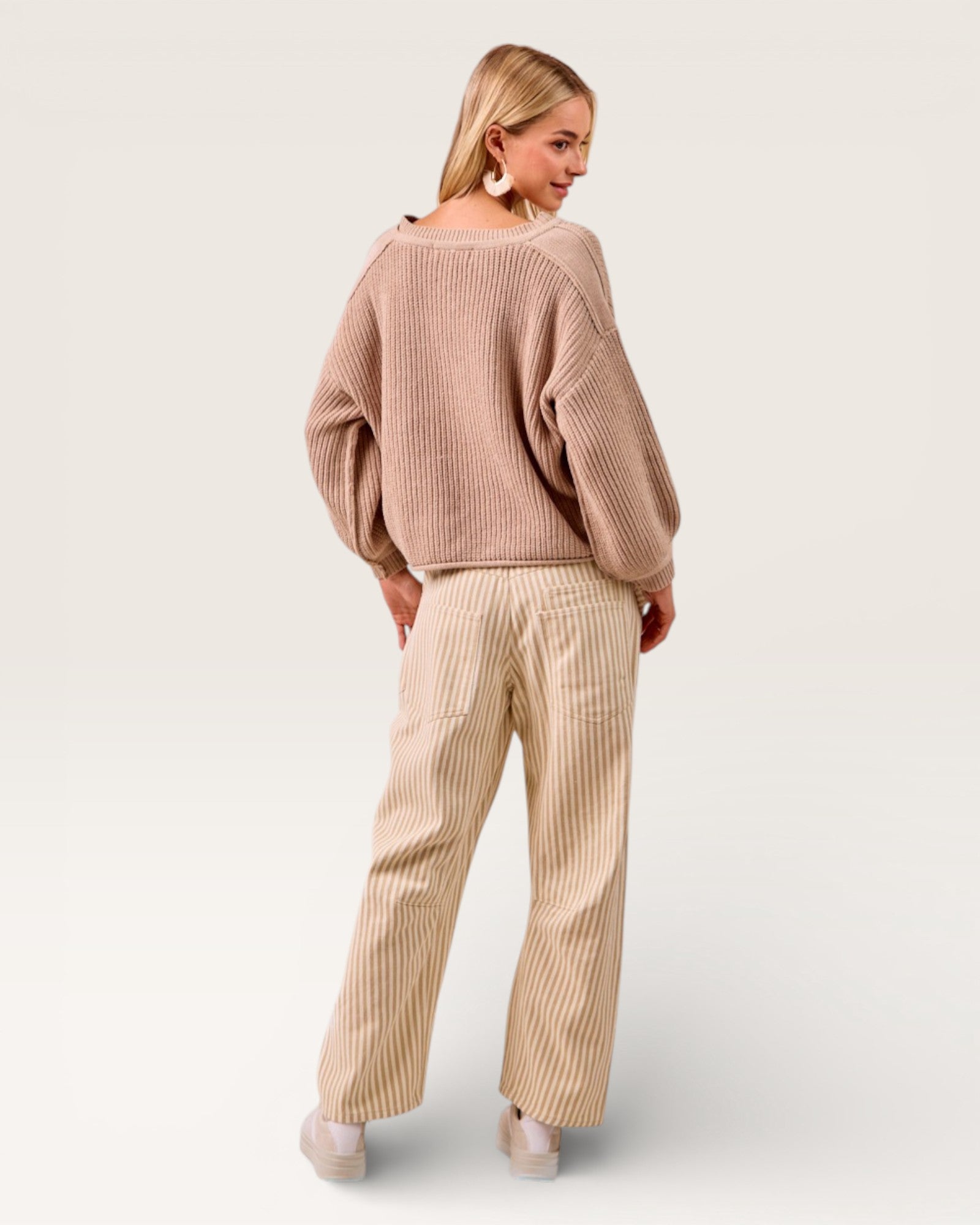 Woman wearing a beige sweater and wide-leg pants on a white background