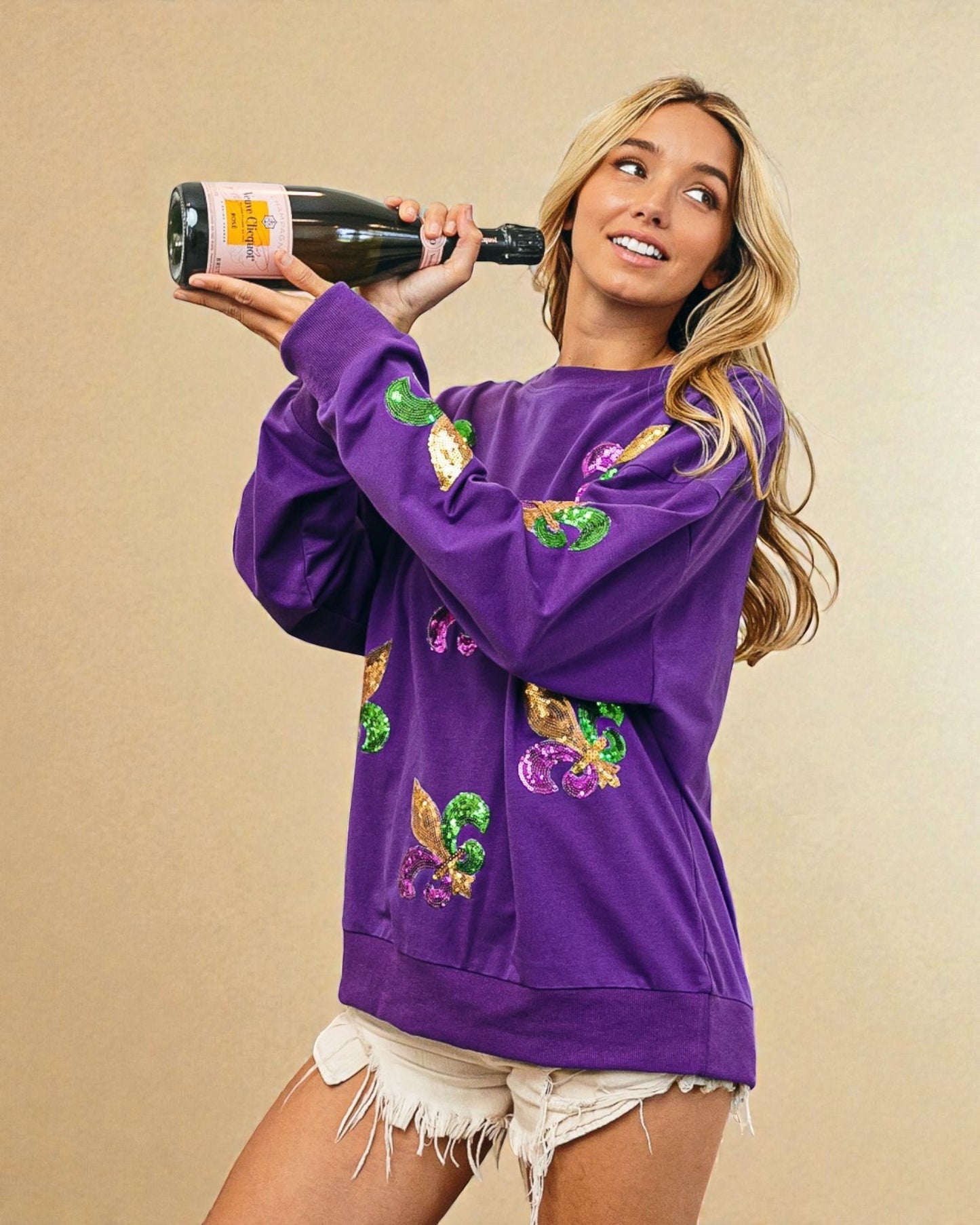 Woman wearing a purple sweatshirt with colorful designs, holding a bottle against a beige background