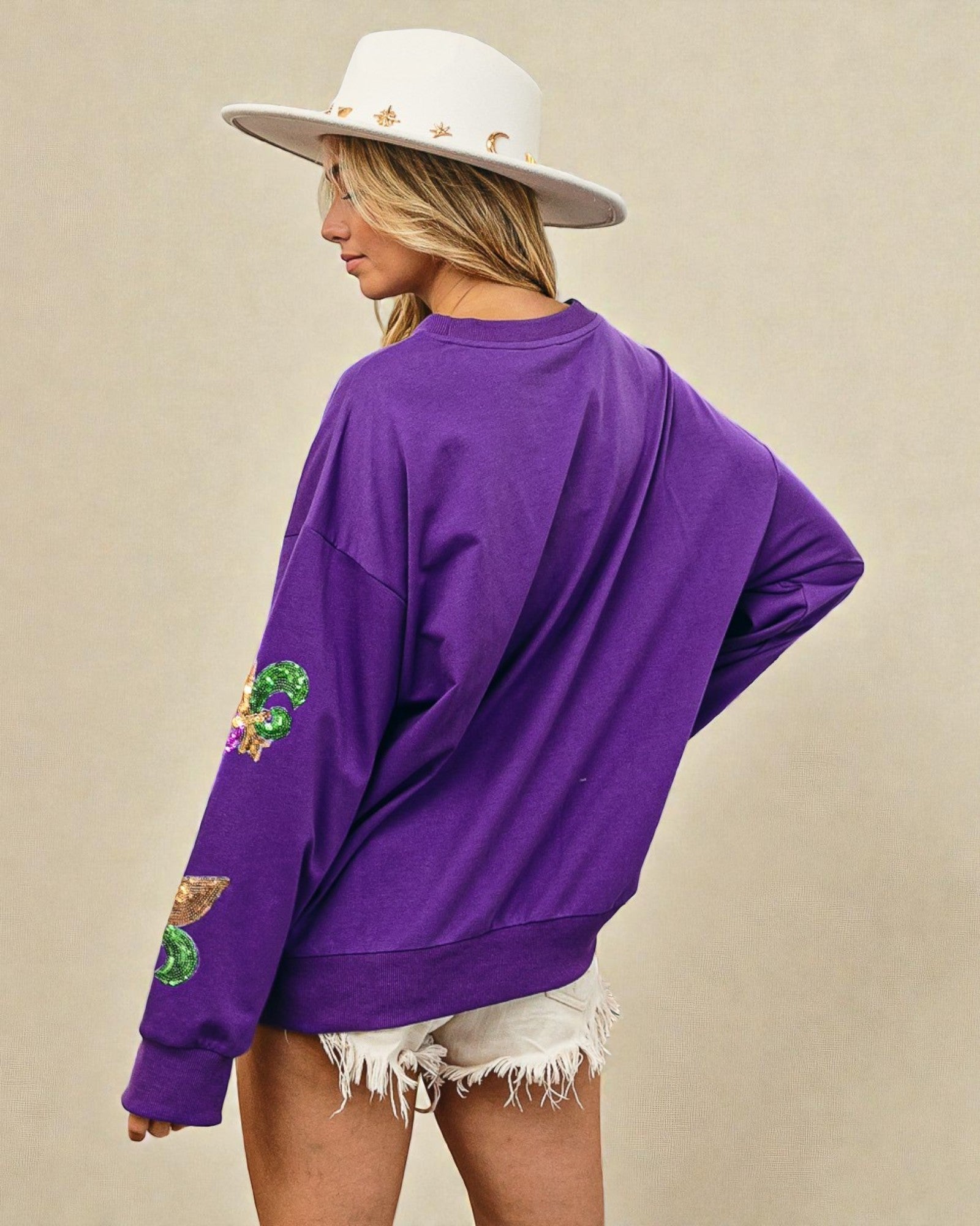 Person wearing a purple sweatshirt with patches on a beige background